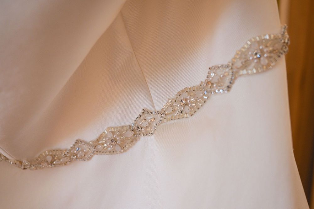 Close-up detail of a delicate crystal beaded belt or sash against white wedding dress fabric.