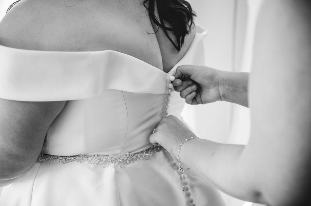 A series of black and white photos showing a bride getting dressed and having her wedding gown laced up.