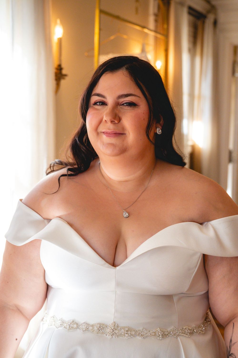 Close-up details of an off-shoulder white wedding dress with sweetheart neckline and crystal belt embellishment.