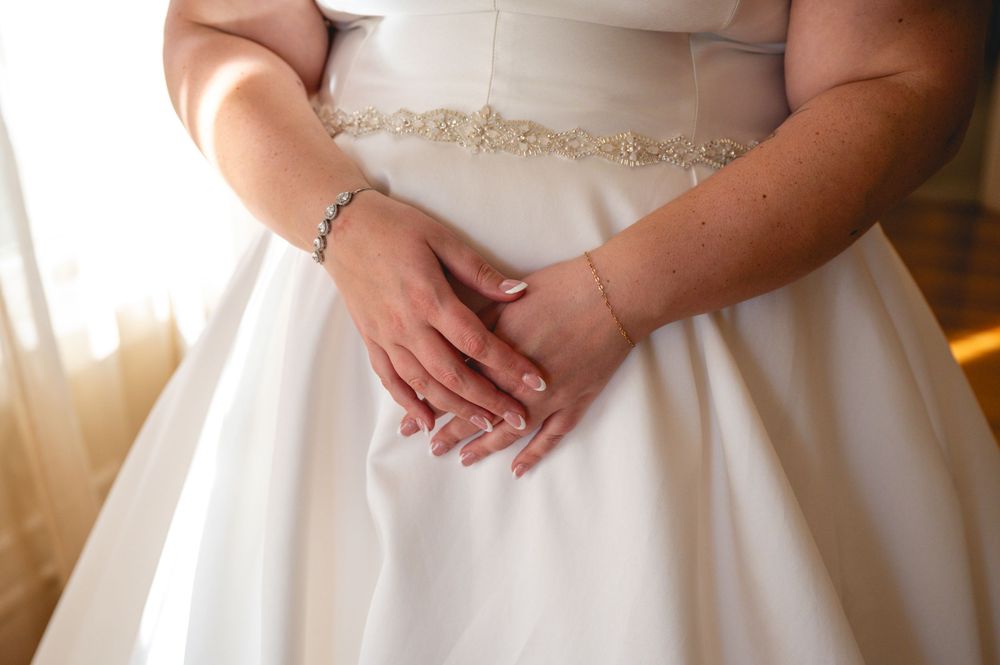 Close-up view of a bride's hands delicately holding her white wedding gown against soft lighting.
