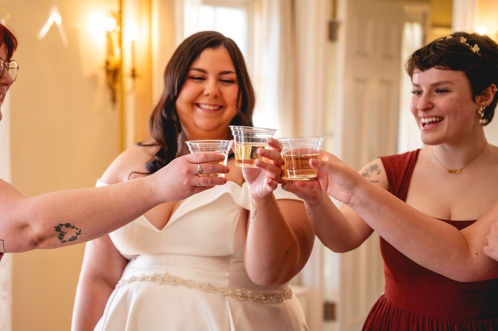 Wedding party members raise their glasses in a celebratory toast at an elegant venue with warm lighting.