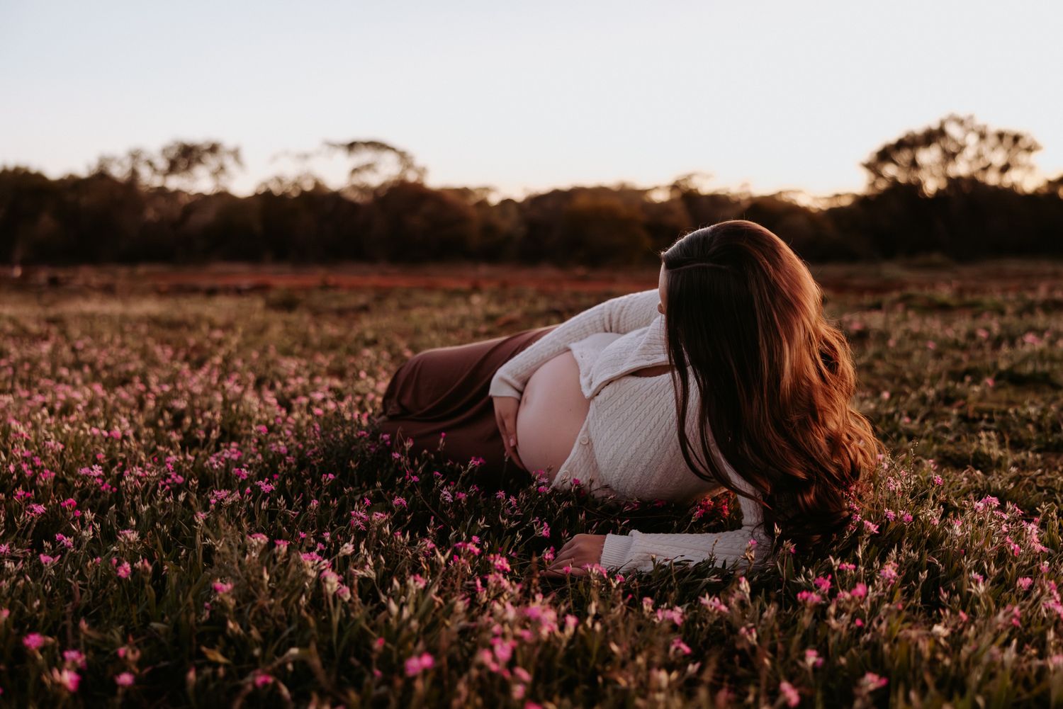 A person lies peacefully in a field of vibrant pink wildflowers at sunset creating a dreamy outdoor scene.