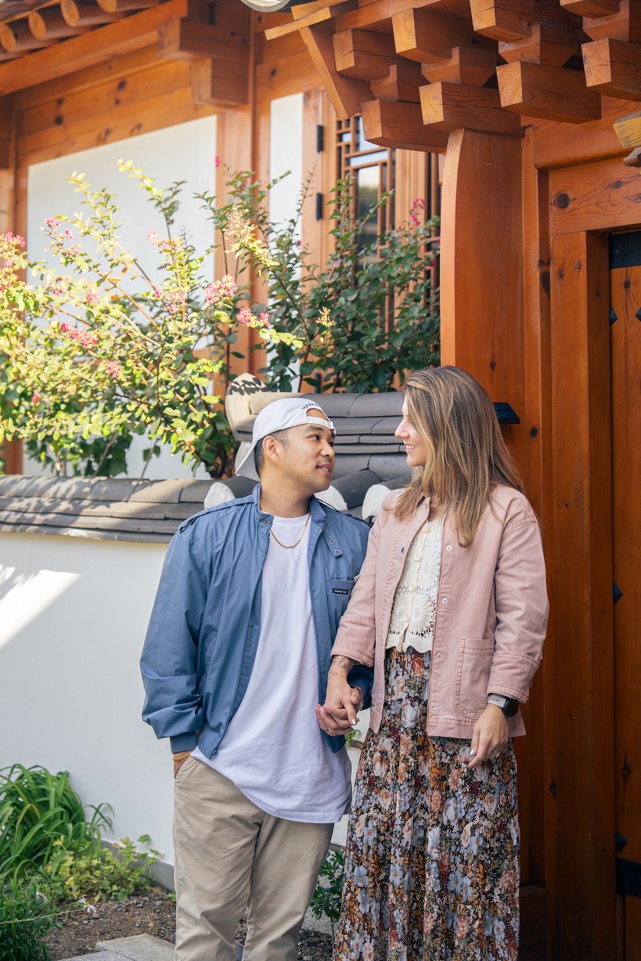 A couple shares a romantic moment under a wooden pergola with blooming flowers in the background.