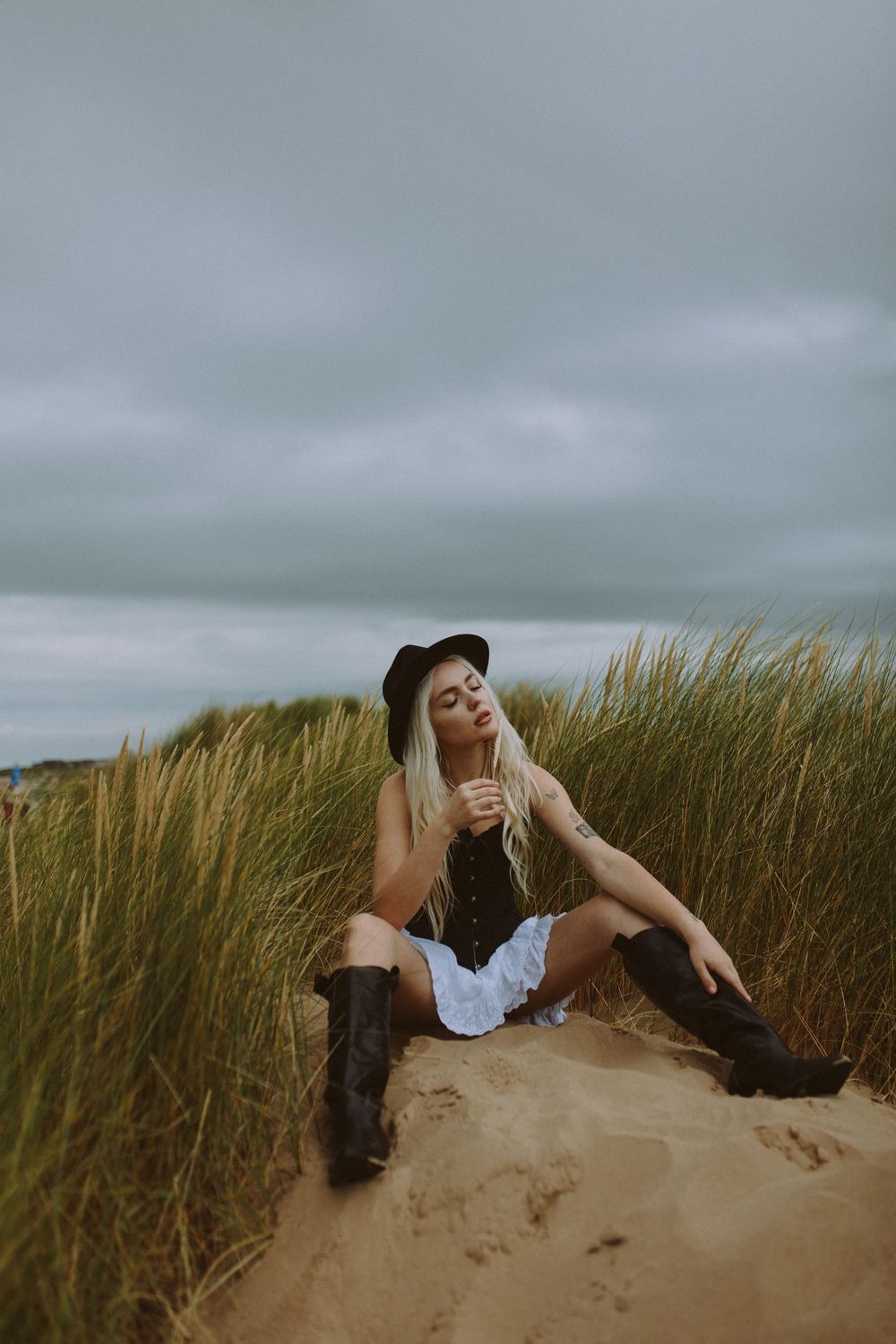 Moody portrait sequence showing dynamic poses on a sandy beach with overcast skies and tall grass.