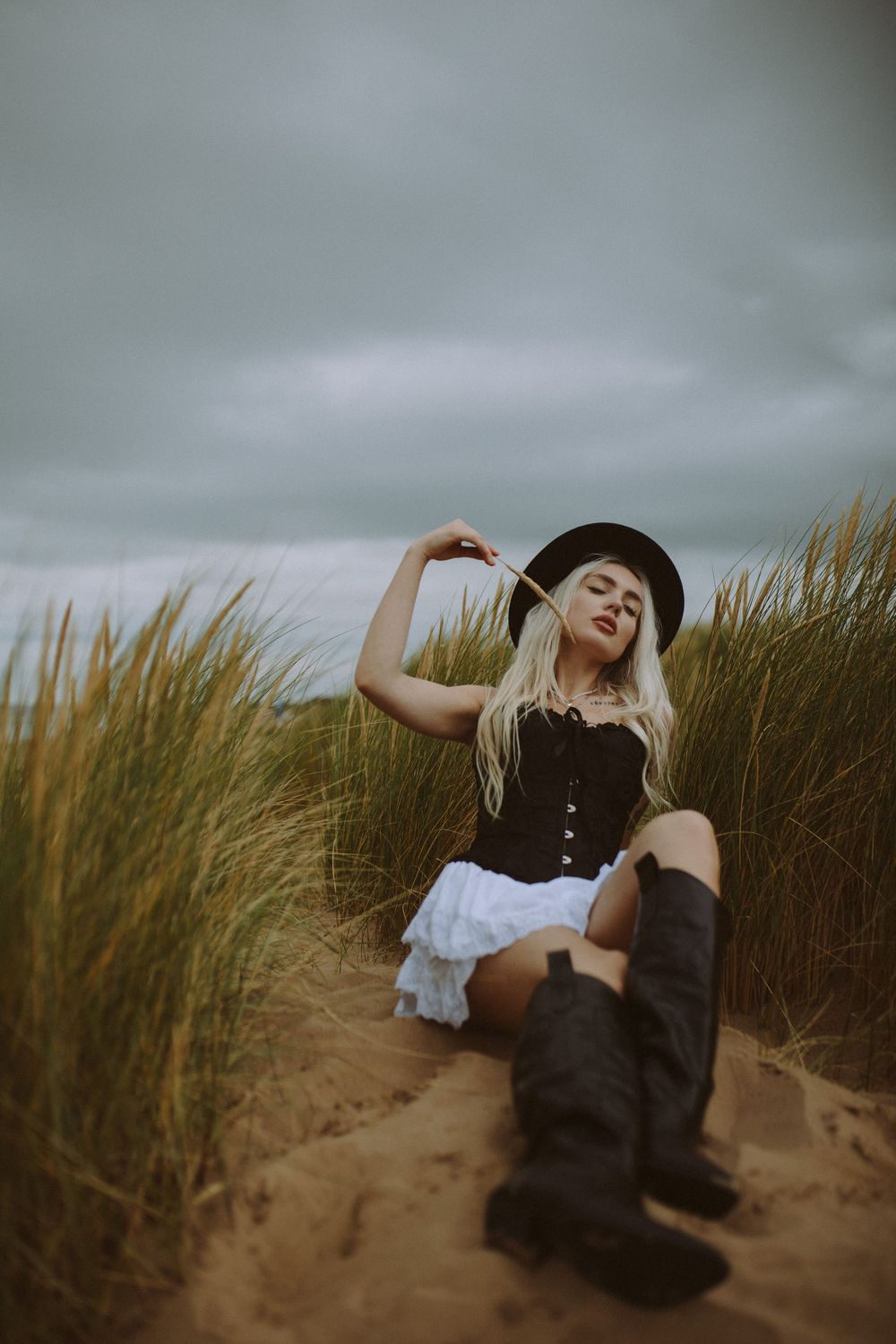 Dramatic poses photographed against cloudy skies and beach grass in a coastal dune setting.