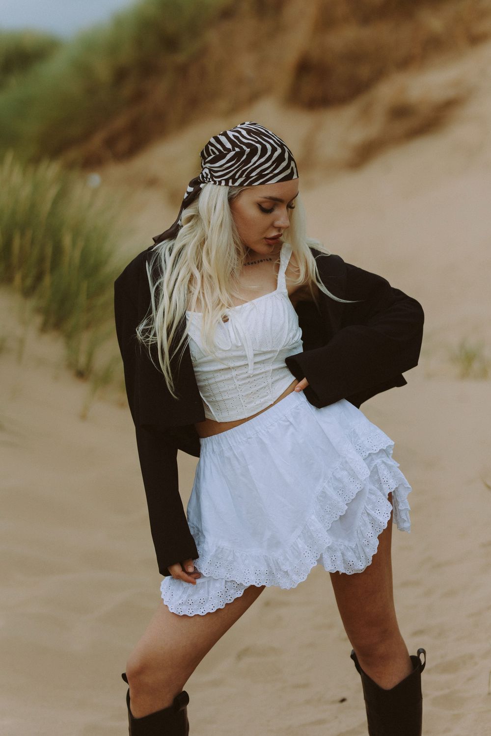 A series of photos showing a person in a white lace dress and black jacket posing on sandy beach dunes at sunset.