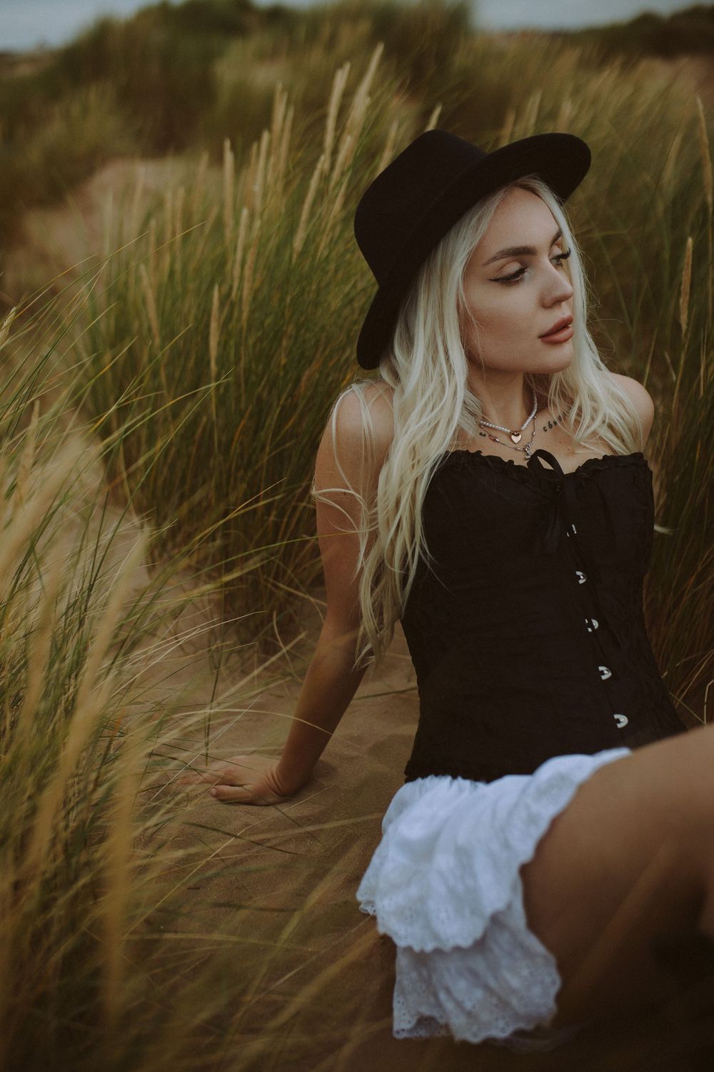 Artistic portrait shots in beach grass showing black clothing and white dress against moody cloudy sky.