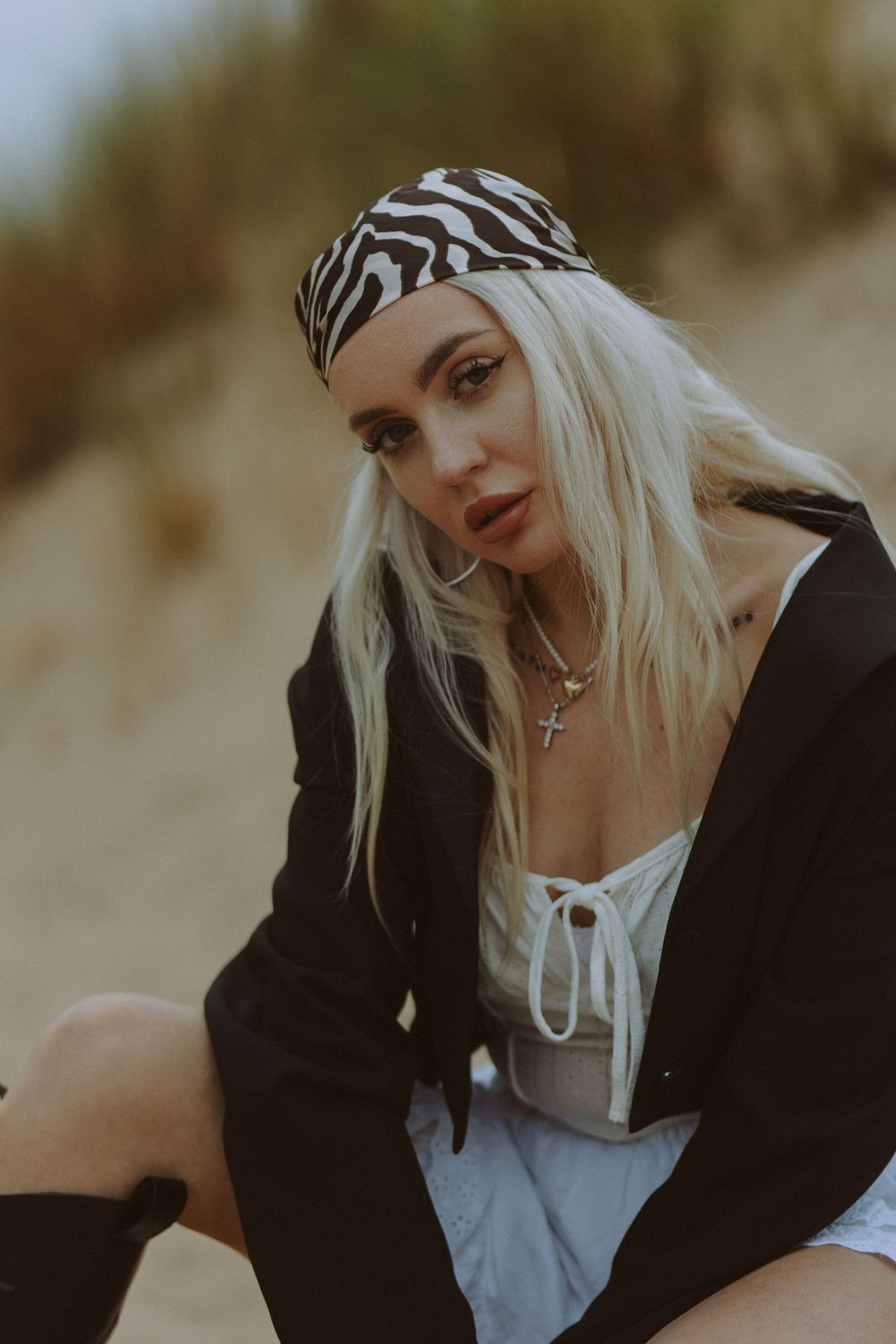 A woman with platinum blonde hair wearing a black jacket and white top poses in a series of artistic outdoor portraits.