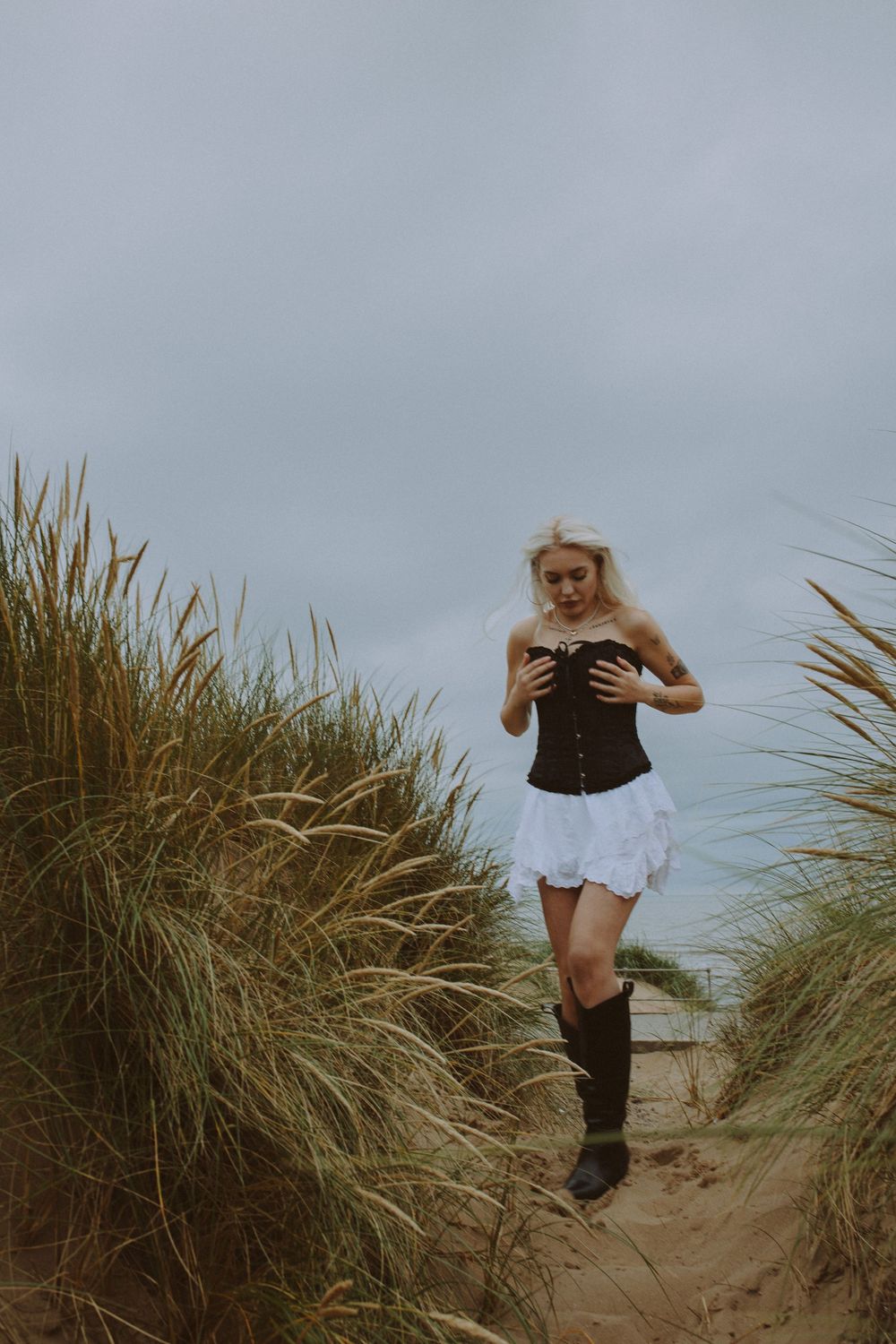 A sequence of photos showing someone jumping and running through beach grass dunes on an overcast day.