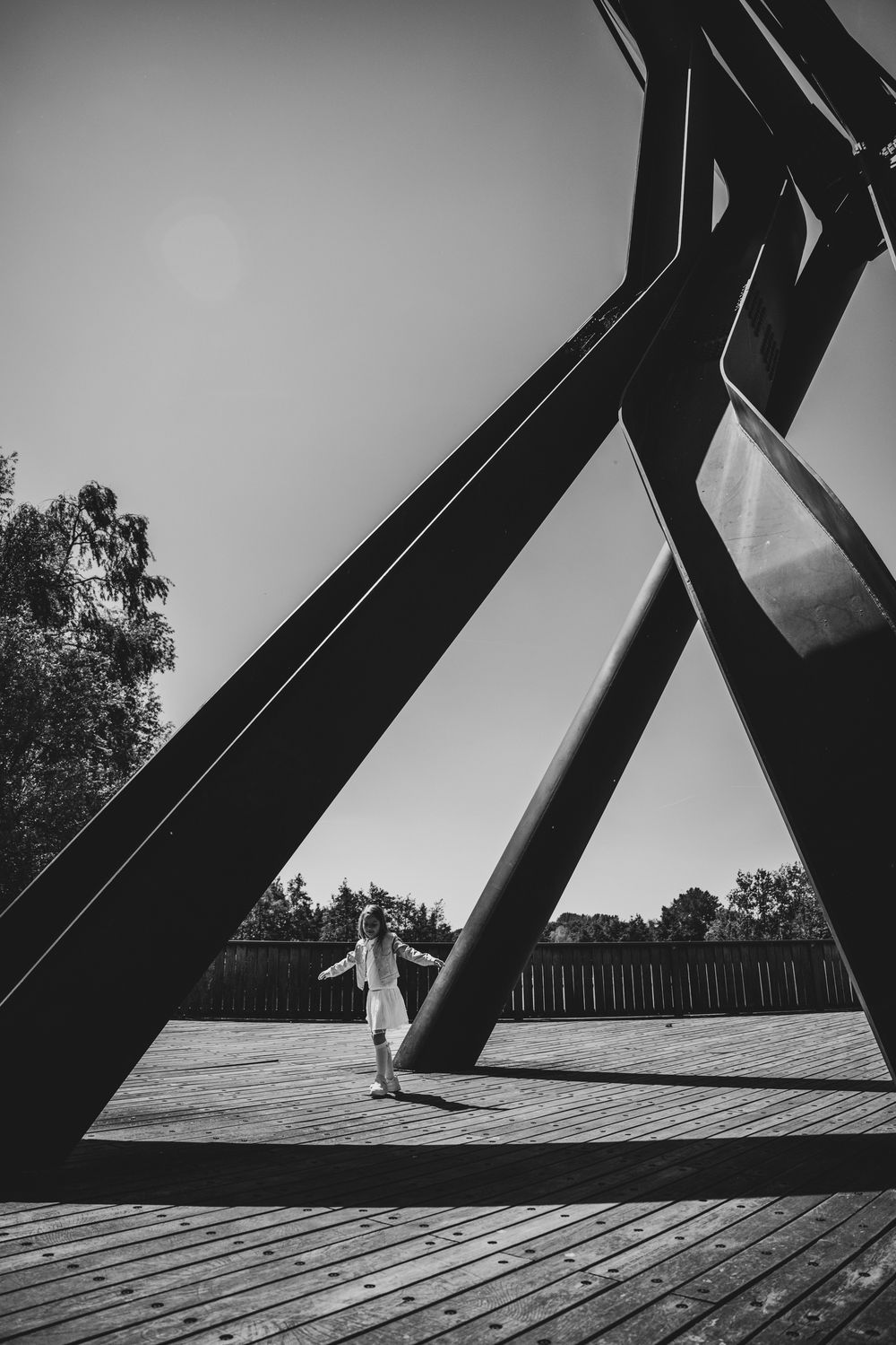 Meisje in witte jurk poseert onder grote metalen constructie – artistieke communie fotografie door Bart Boodts