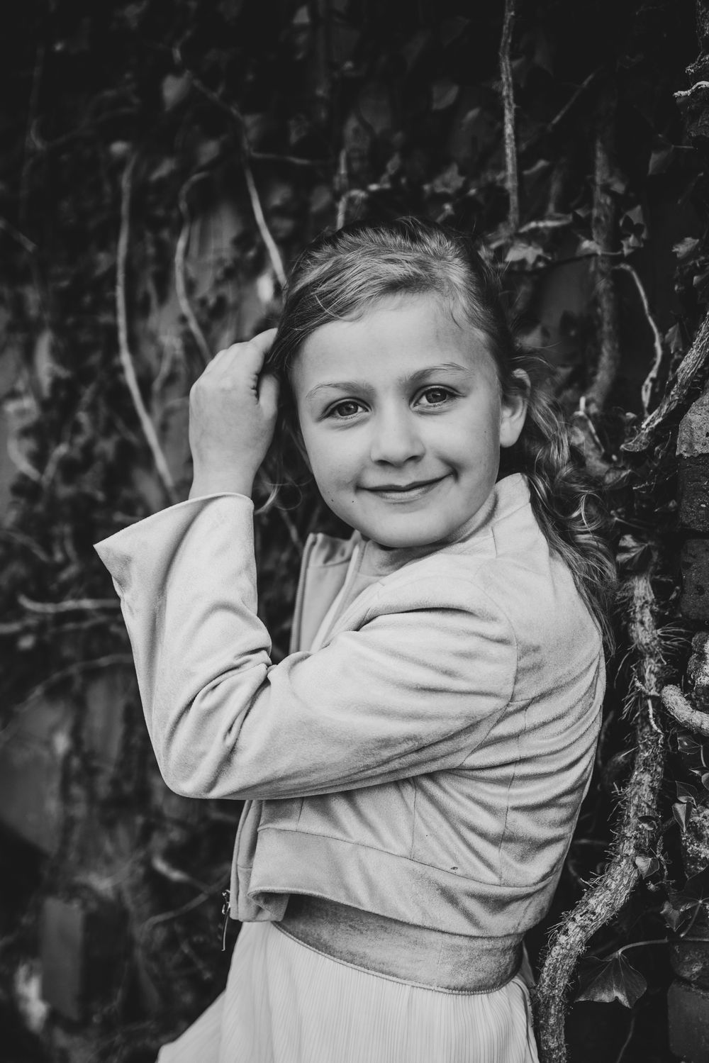 Zwart-wit portret van meisje dat glimlacht bij oude muur – tijdloze communiefotografie door Bart Boodts Photography