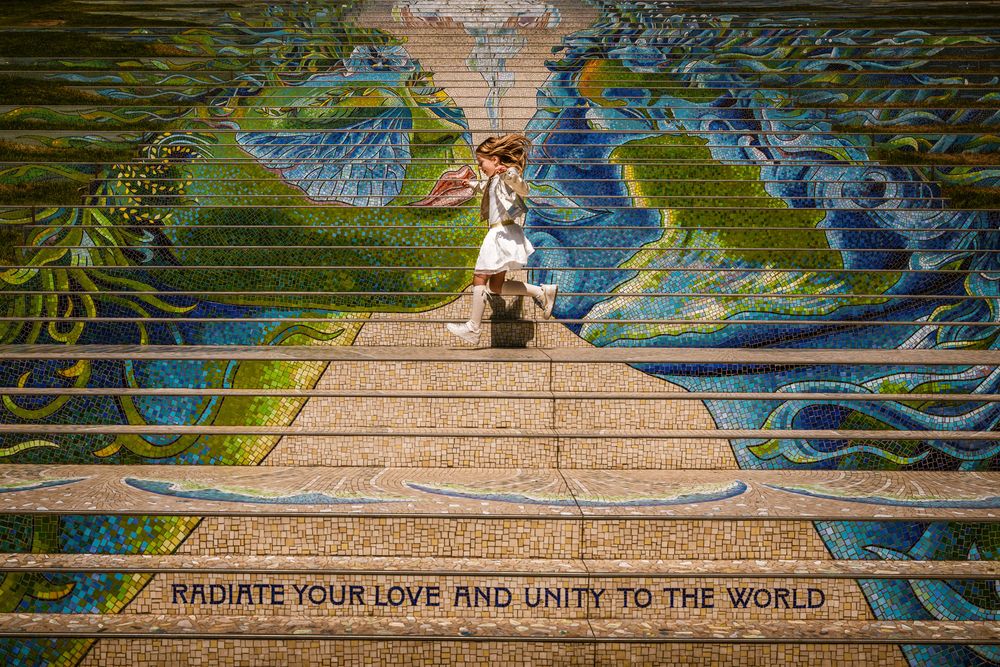 Meisje rent over kleurrijke mozaïektrap met boodschap “Radiate your love” – creatieve communie fotografie door Bart Boodts