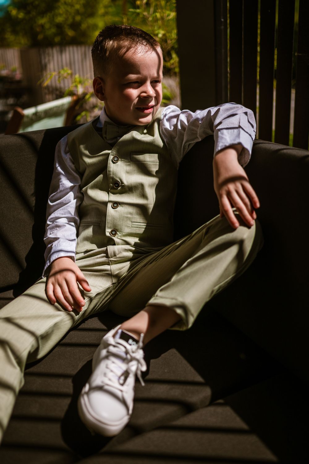 Jongen in groen kostuum geniet van zonlicht tijdens ontspannen communieportret – sfeervolle reportage door Bart Boodts Photography