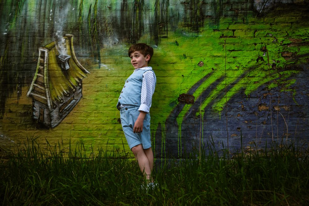 Jongen in lichtblauw kostuum poseert speels tegen felgroene muurschildering tijdens creatieve communieshoot – Bart Boodts Photography