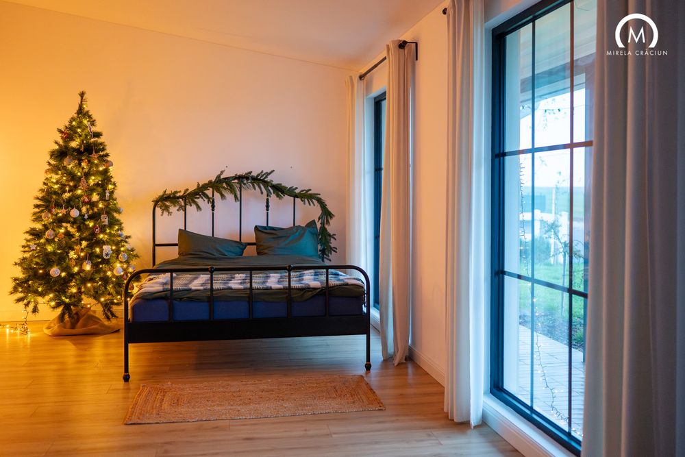 A cozy bedroom with a lit Christmas tree, metal bed frame, and large glass sliding doors leading to a balcony.