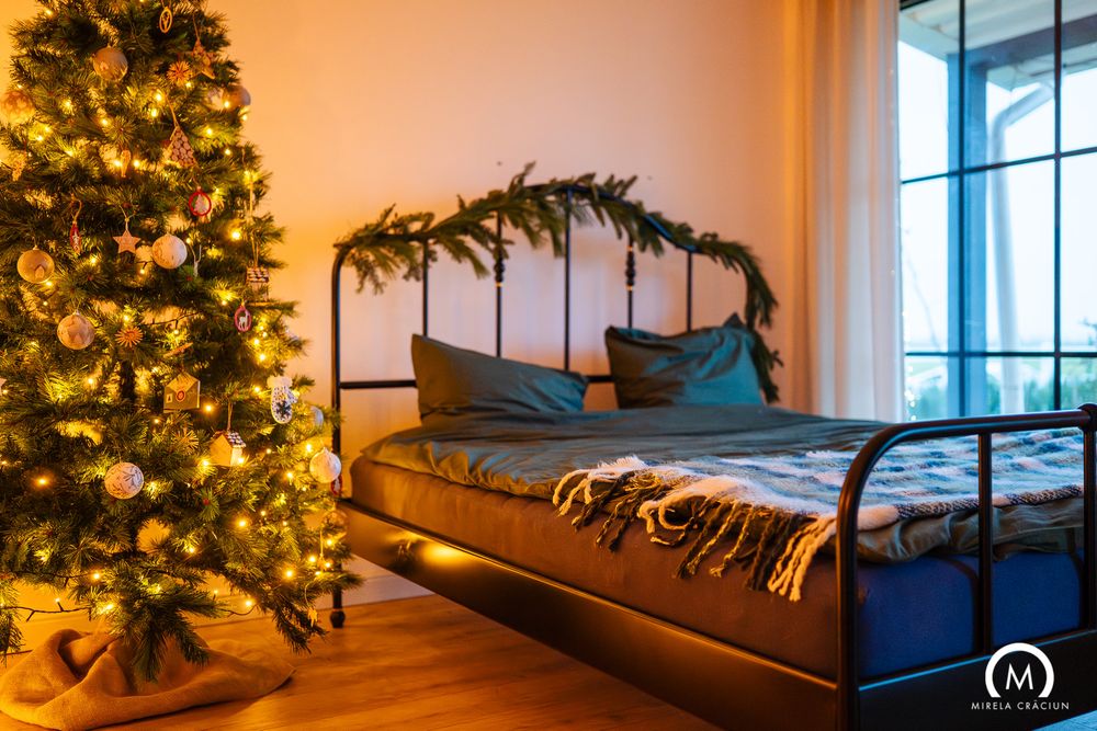 A cozy bedroom decorated for Christmas with a lit tree, window, and blue bedding creating a warm holiday atmosphere.