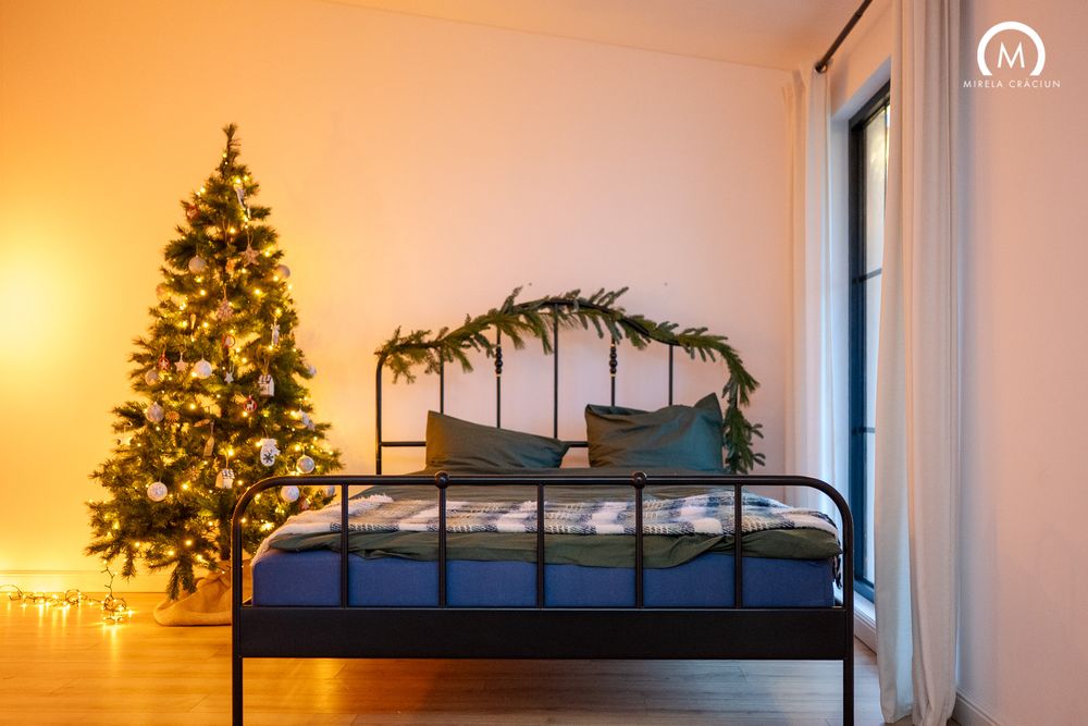 A cozy bedroom with a lofted bed and Christmas tree silhouetted against a warm orange sunset through the window.