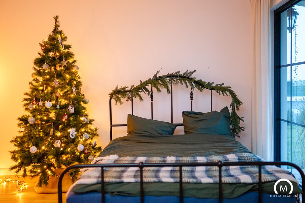Cozy bedroom with decorated Christmas tree and metal bed frame adorned with garland and warm lighting.