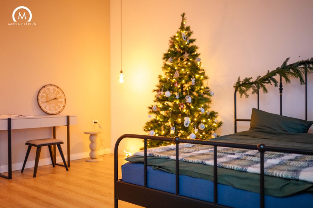 A cozy bedroom interior with a decorated Christmas tree glowing warmly in the corner near a bed.