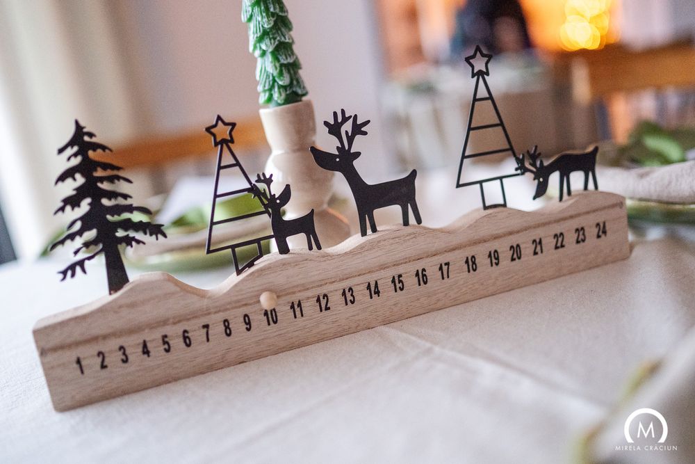 Wooden calendar display with decorative winter scene silhouettes featuring trees and reindeer against white background.