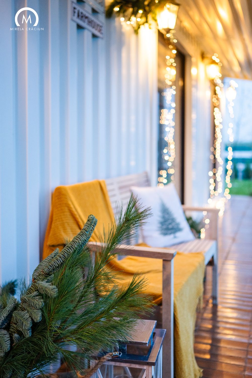 White columns line a festive porch decorated with twinkling Christmas lights and evergreen garlands at dusk.