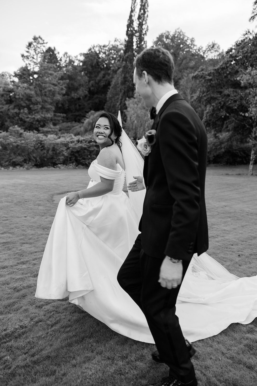 A couple in wedding attire dances playfully outdoors as the bride's white dress flows in the wind.