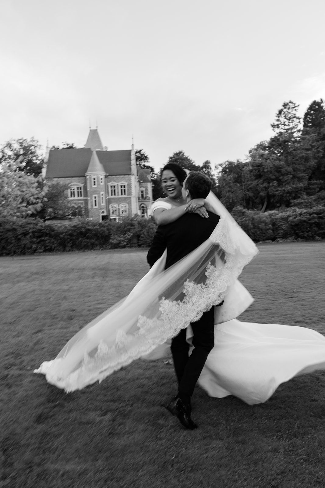 A couple dances on a lawn with a flowing white wedding dress creating elegant movement in black and white photography.
