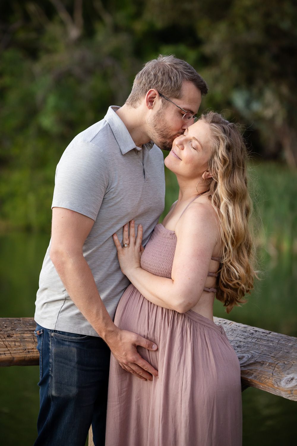 A couple share a kiss in a romantic outdoor maternity photoshoot on a wooden pier