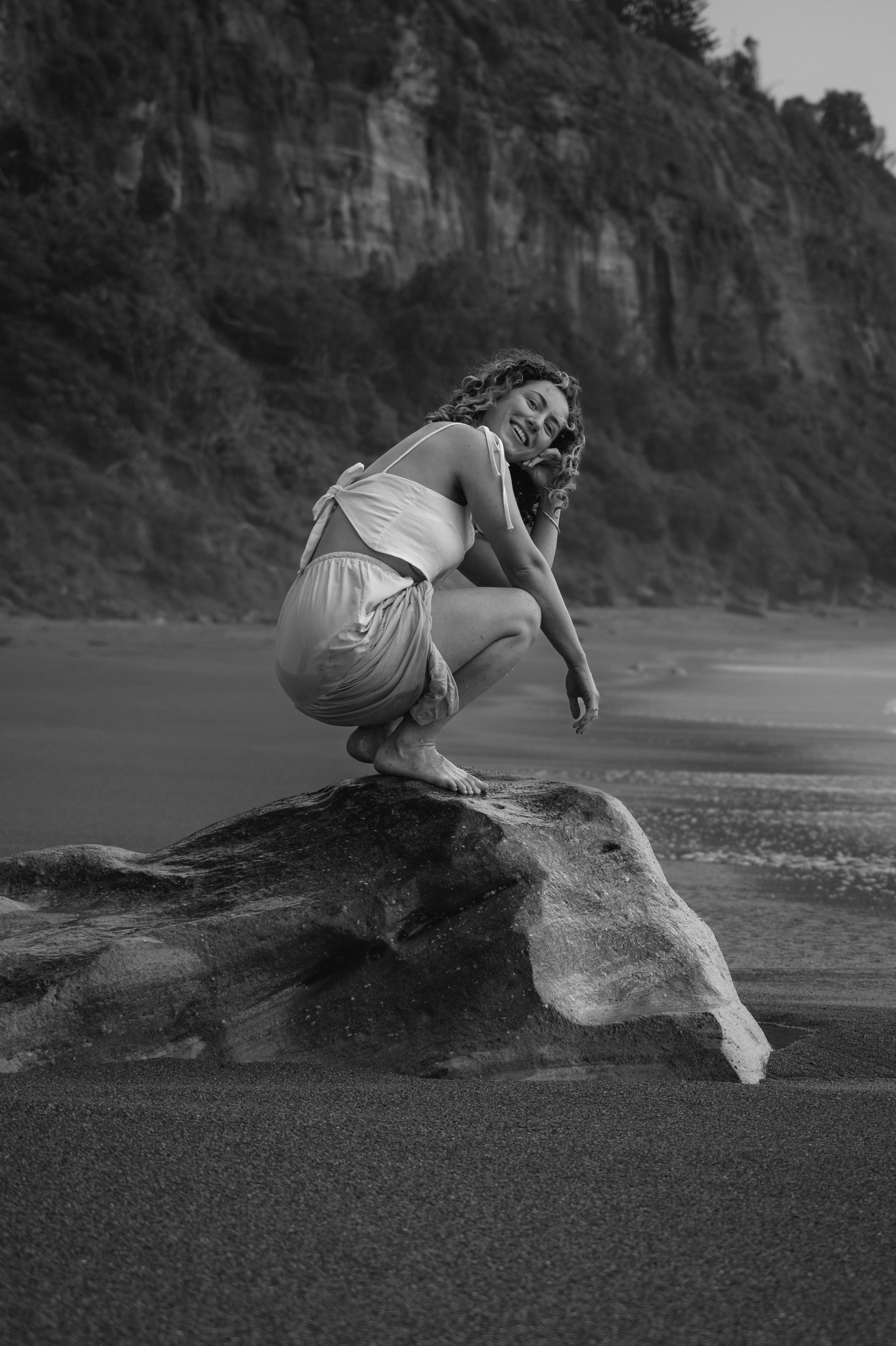 A dramatic black and white photo captures movement on a sandy beach against towering cliffs.