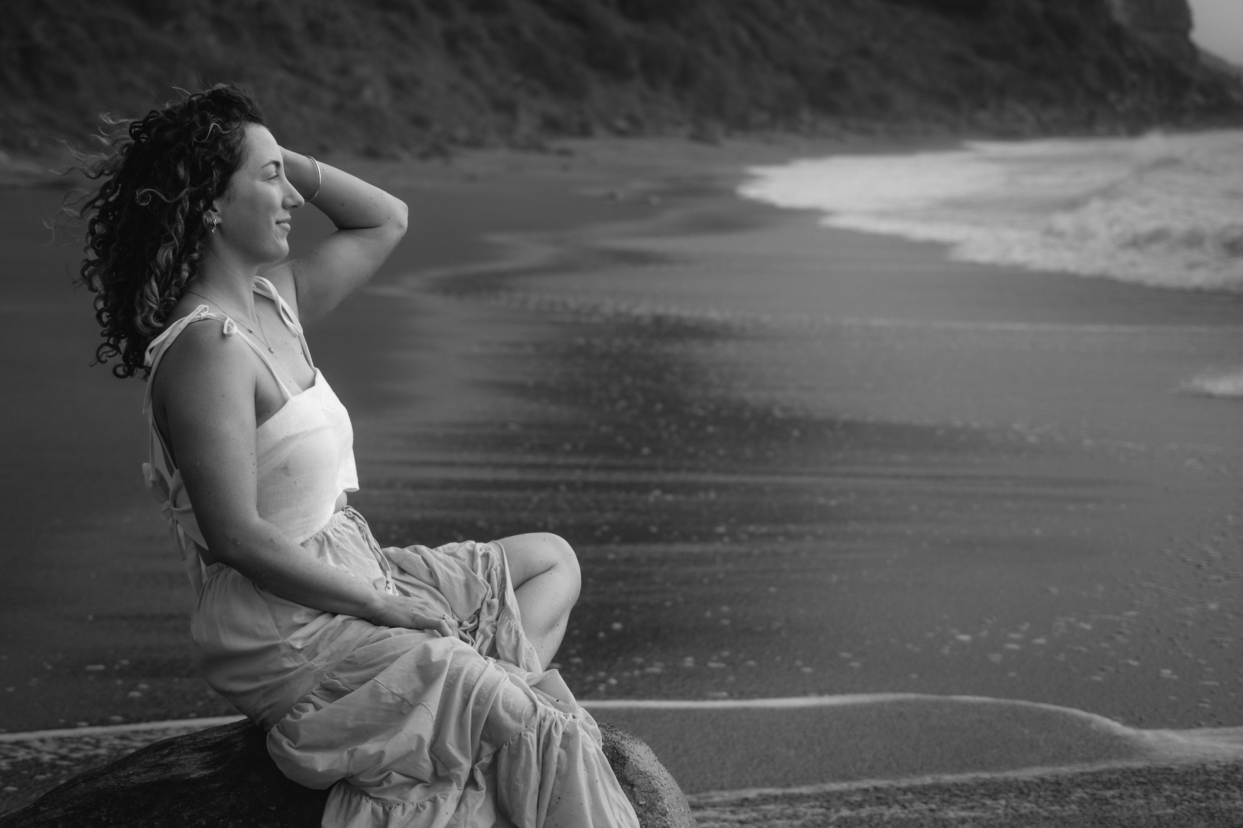 A black and white artistic photo series shows someone in a flowing dress sitting by water in different poses.