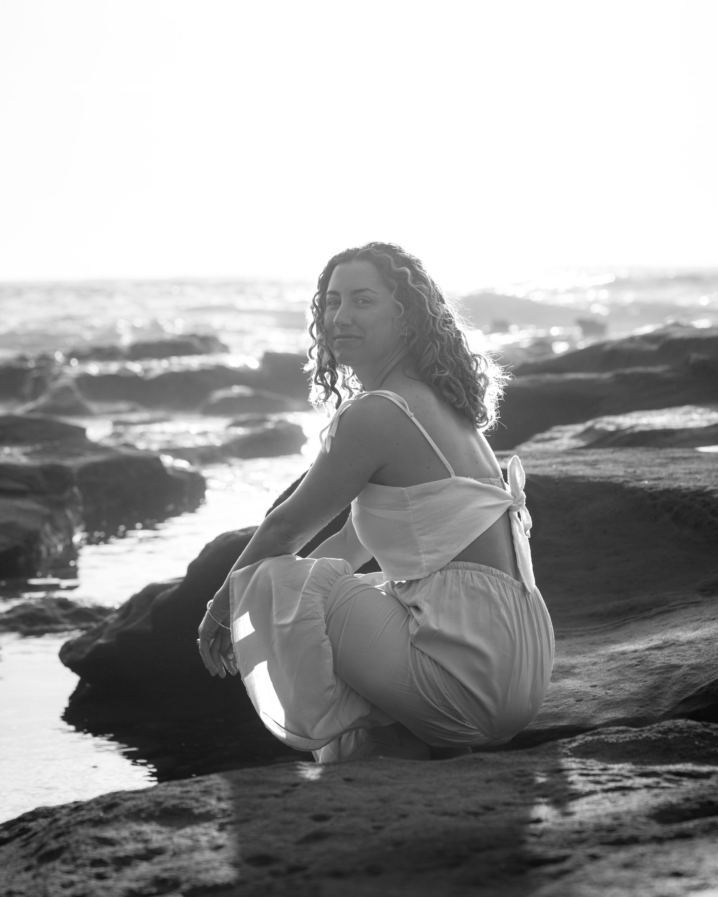 A person in white clothing reclines on dark coastal rocks at sunset in a series of artistic black and white photographs.