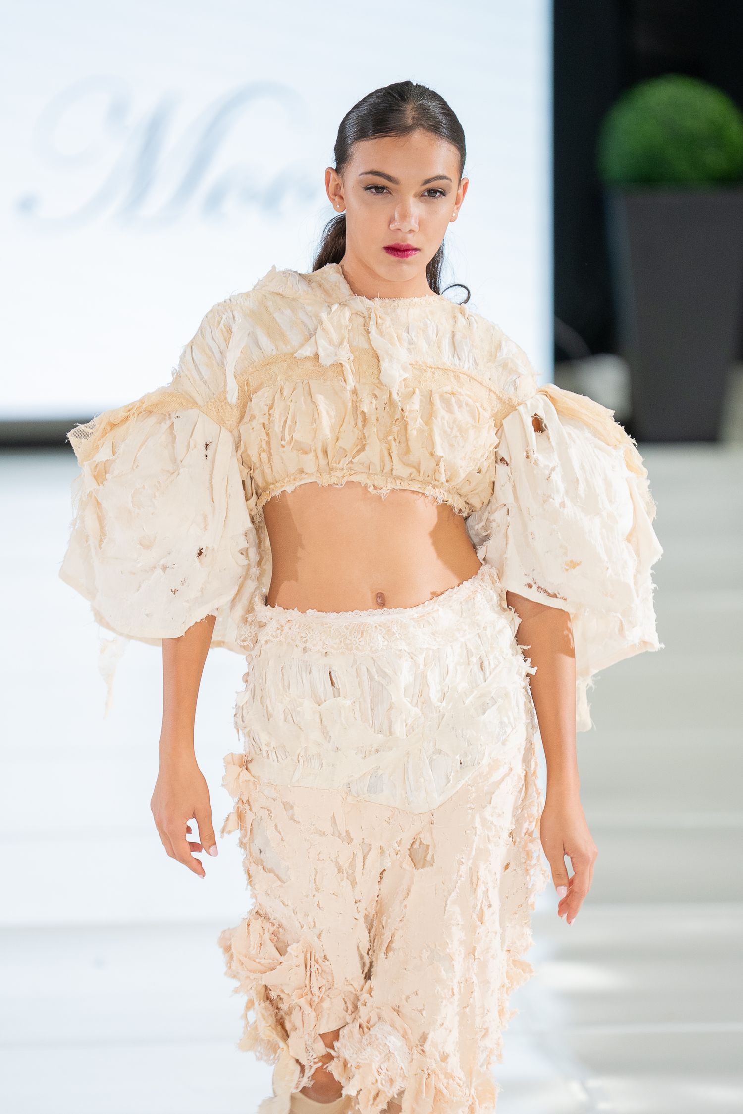 Fashion model walks runway in dramatic cream-colored ruffled dress with statement puff sleeves during fashion show.
