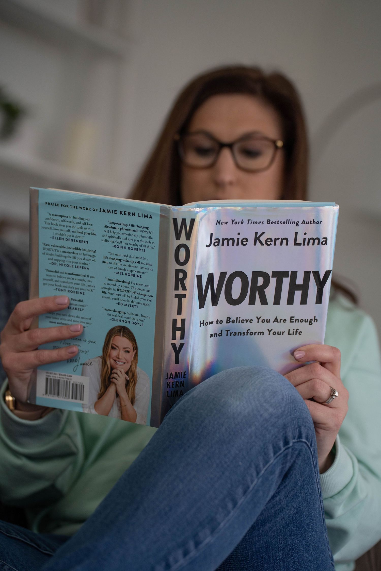 Reading self-help book titled 'Worthy' while relaxing in casual home setting.