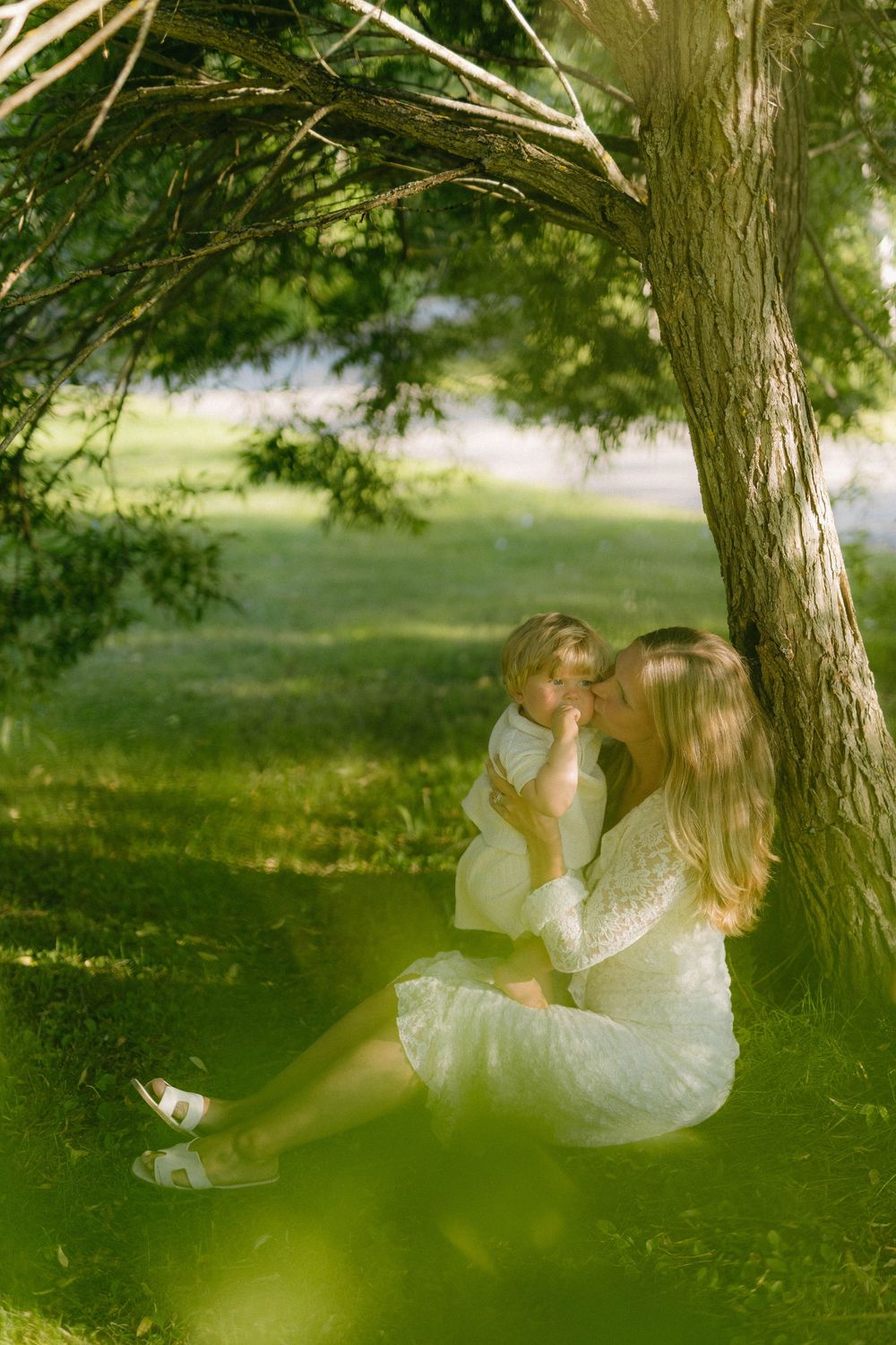 A romantic couple in white dress embraces under a tree in a dreamy outdoor setting during a summer day.