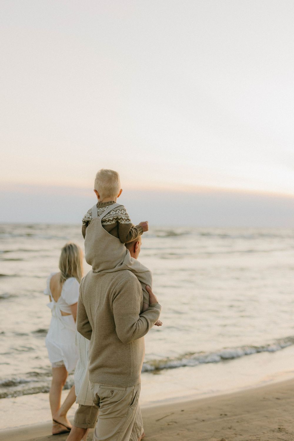 Family walking along a scenic beach at sunset with gentle waves and golden light creating a peaceful atmosphere.