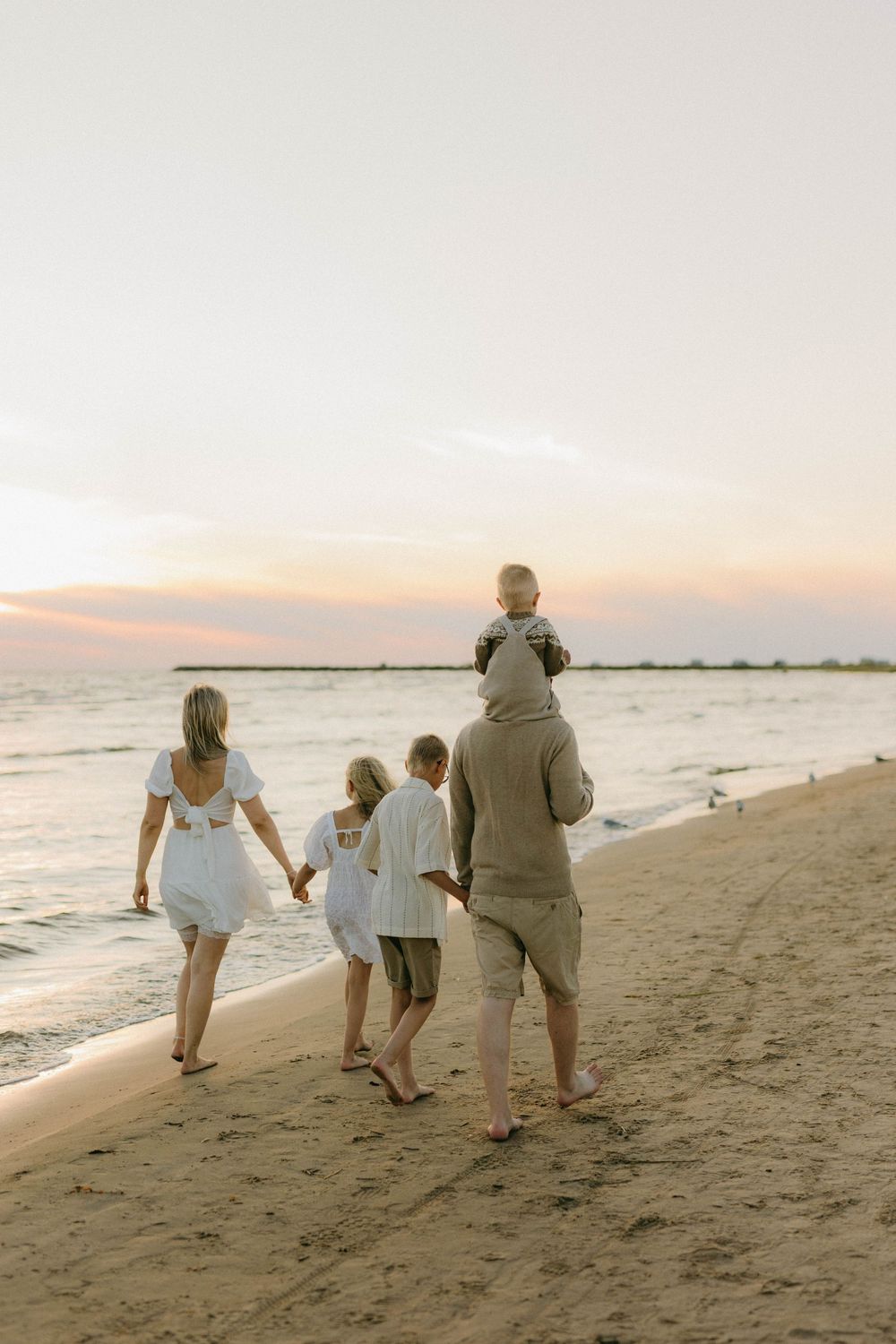 A family walks together along a peaceful beach at sunset, enjoying a serene moment by the ocean.