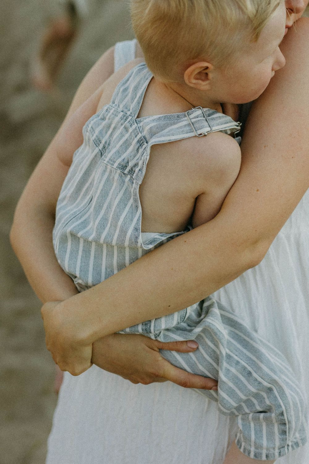 Close-up sequence showing gentle embrace between parent and baby wearing striped romper against neutral background.