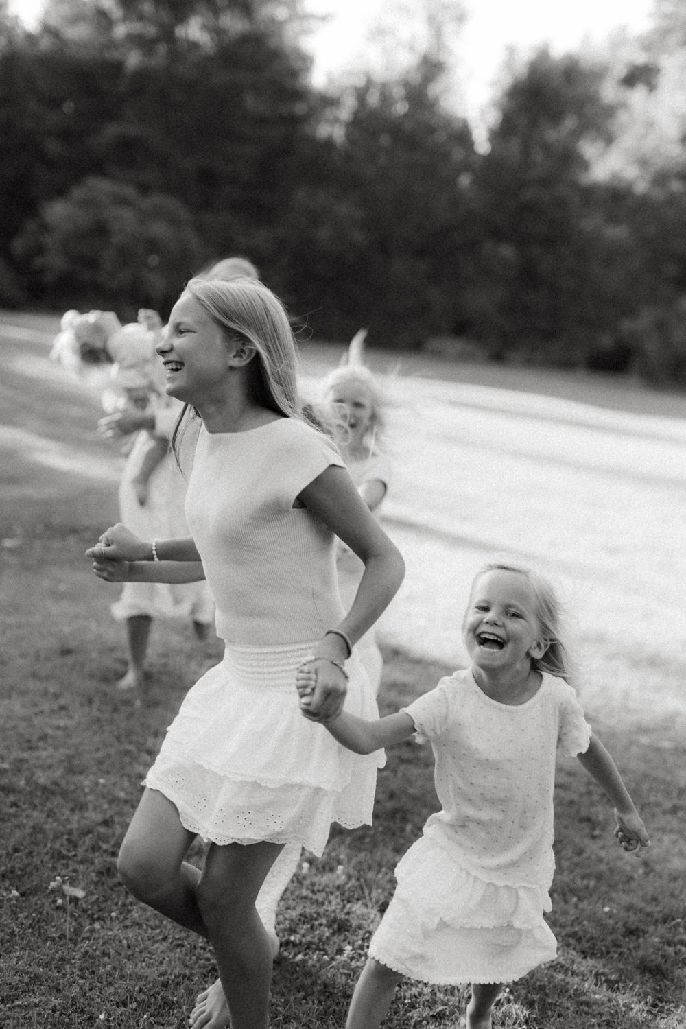 A joyful black and white photograph shows people in white dresses running and playing together outdoors.
