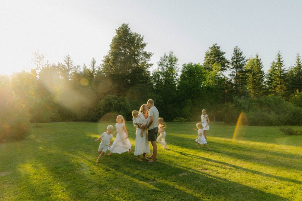A family walks together through a sunlit meadow at golden hour as sunbeams illuminate the grassy landscape.