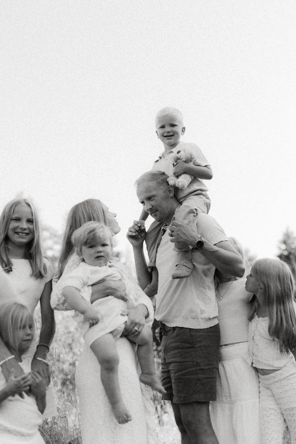 A joyful black and white family portrait outdoors showing children and adults gathered together in a candid moment.