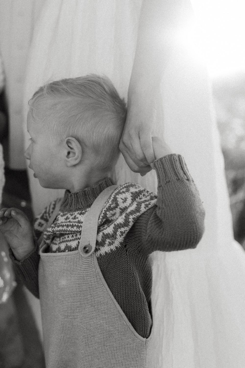 Black and white sequence of a baby in a knit sweater peeking through white curtains.