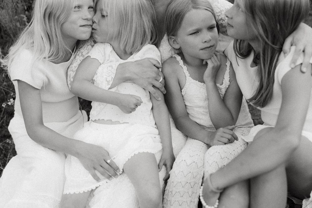 A series of black and white photographs showing tender moments between parents and children in matching white outfits.