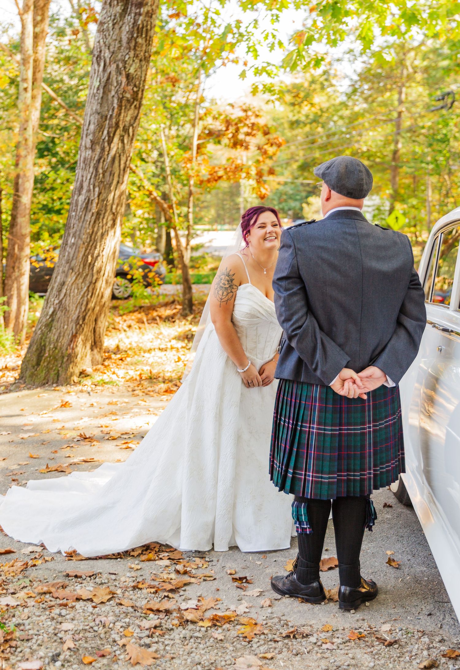 A couple in wedding attire shares a playful moment in a wooded outdoor setting during autumn.