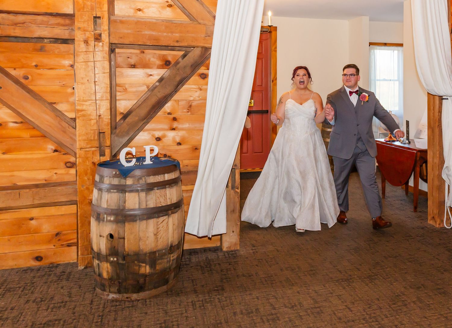 A rustic barn wedding venue interior with white drapes, wooden walls, and a decorative whiskey barrel.