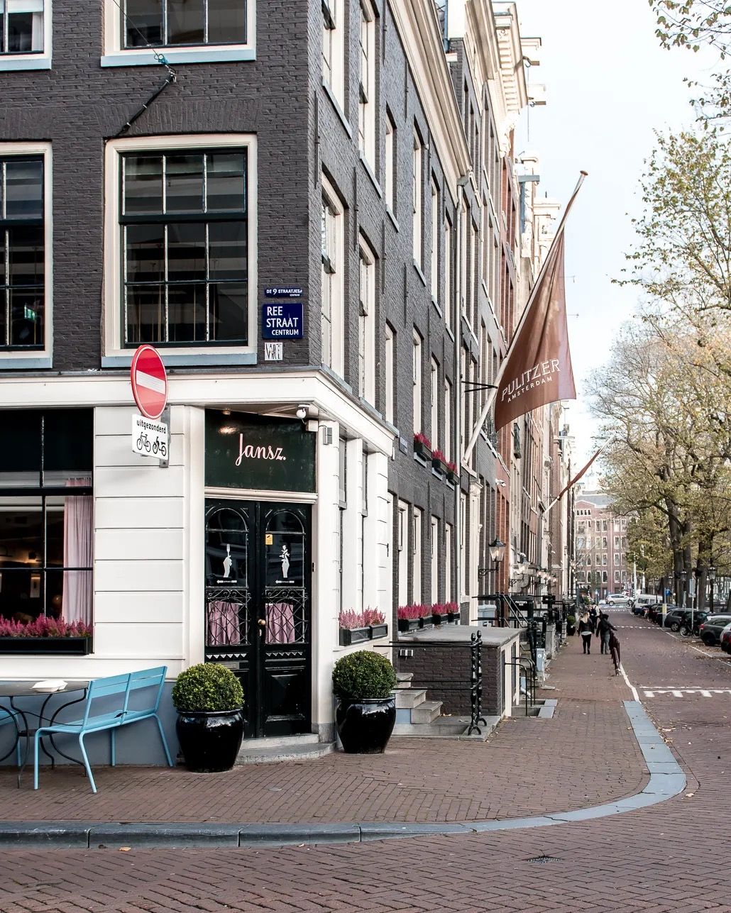 Historic Amsterdam corner building on a quiet street lined with trees and parked bicycles.