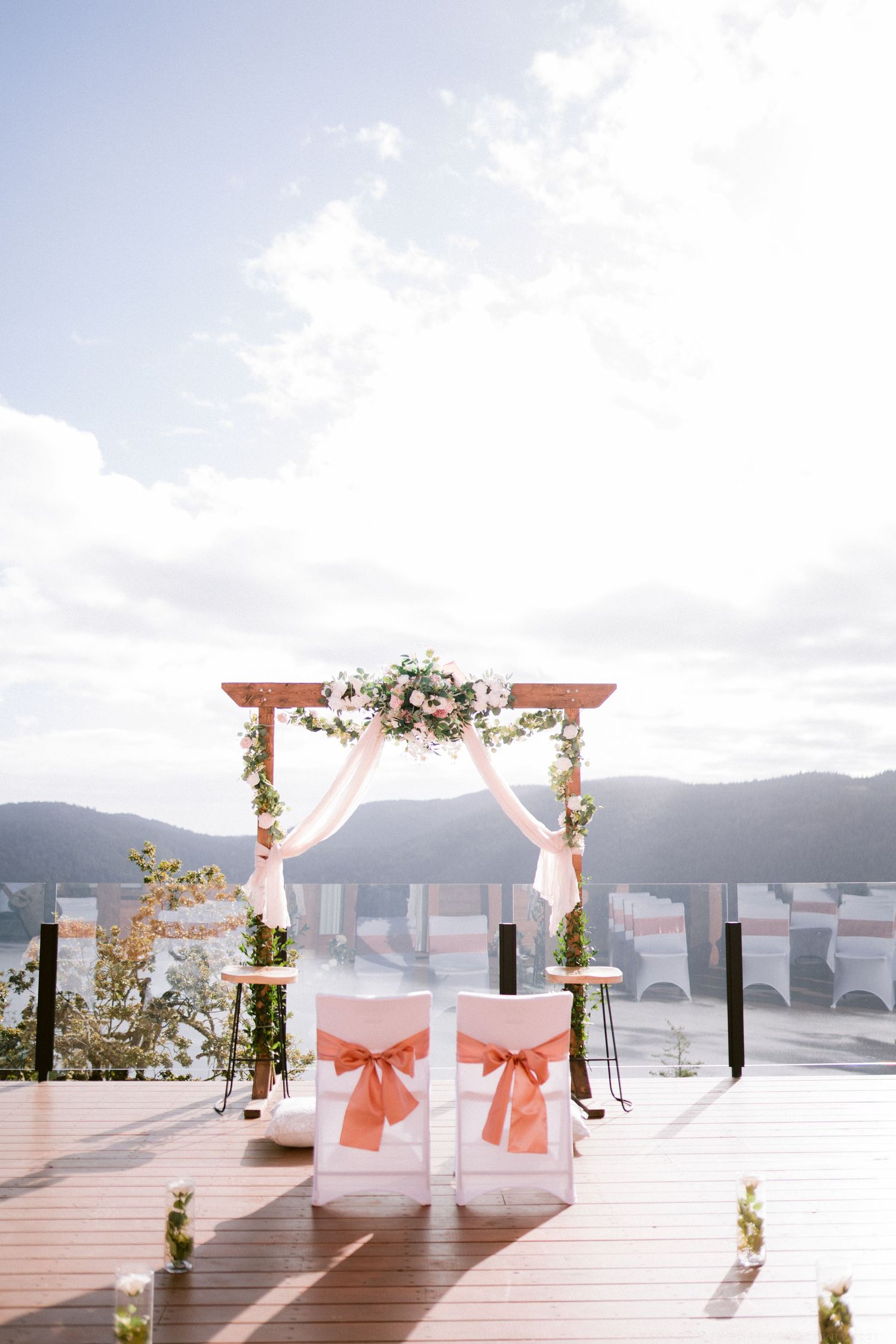 Waterfront wedding ceremony setup with coral ribbons and floral arrangements on wooden dock.