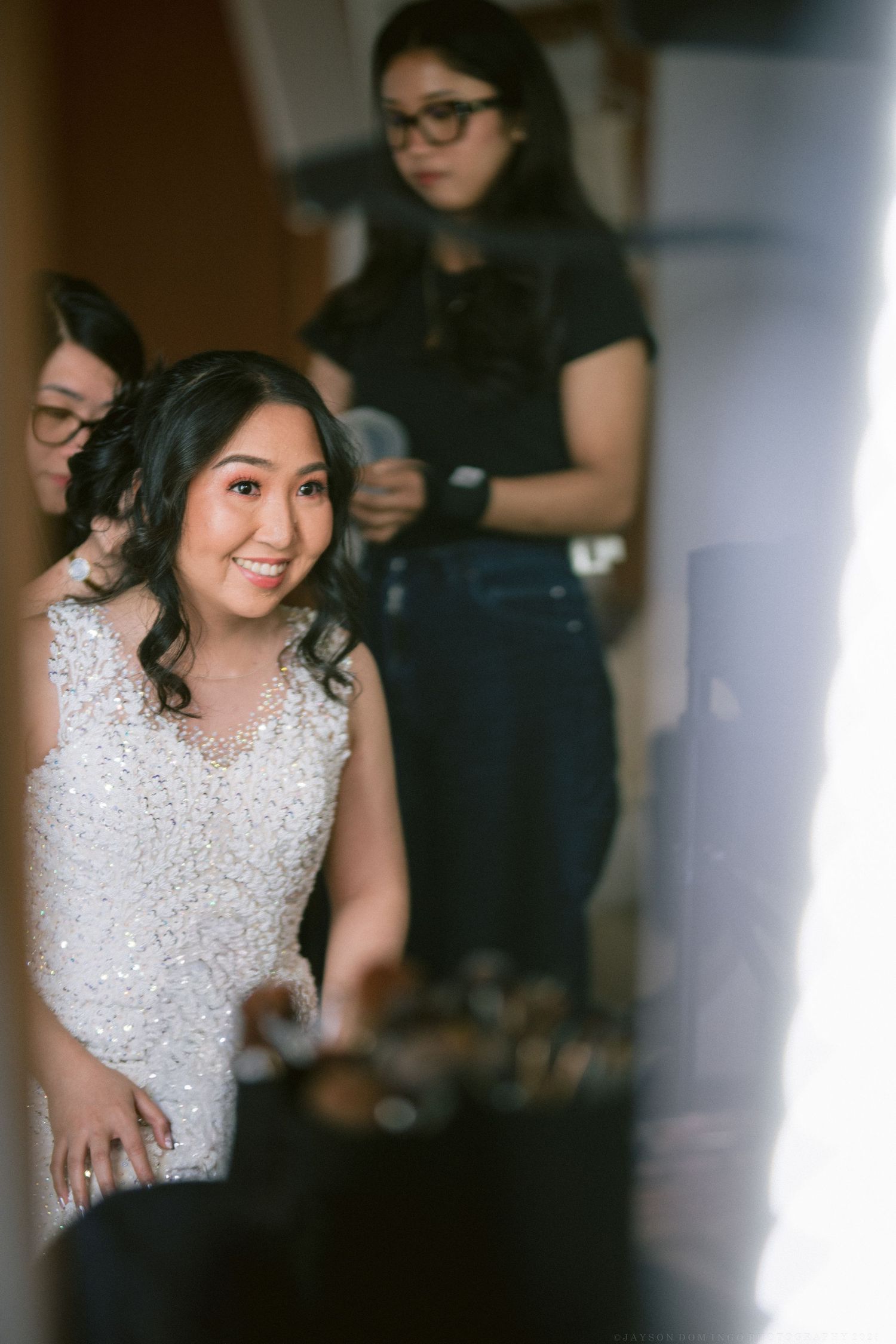 Bride getting ready with a radiant smile while wearing a sparkling beaded wedding dress.
