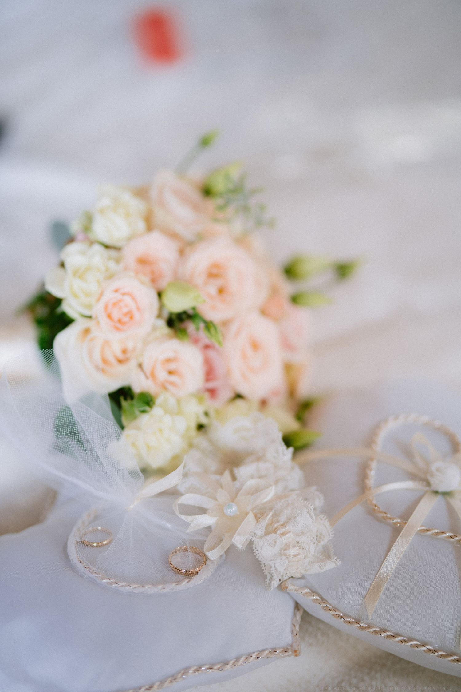 Delicate pink and white roses with wedding rings arranged on white fabric with decorative string accents.