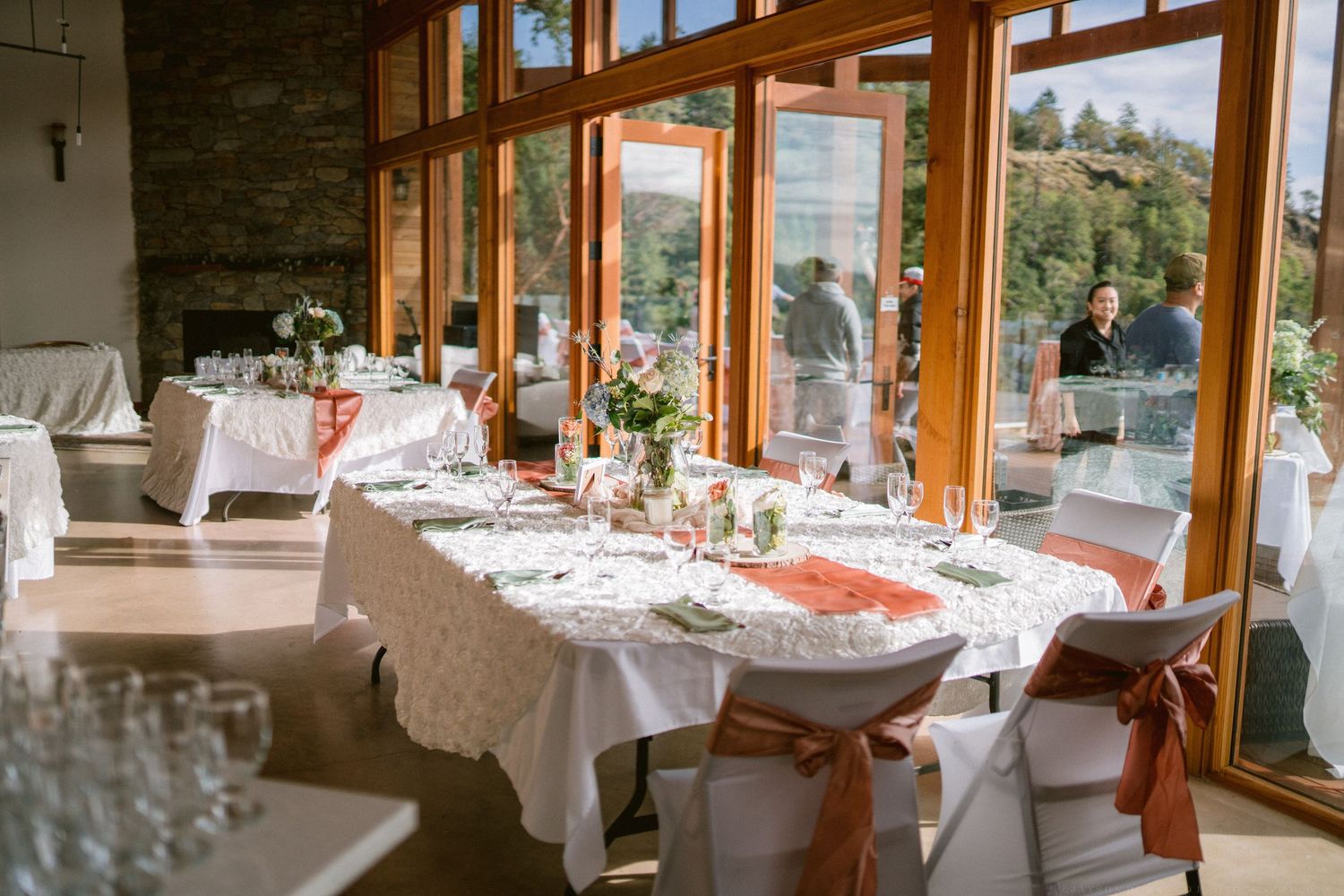 Wedding reception tables set with white linens and decor in a room with mountain views.