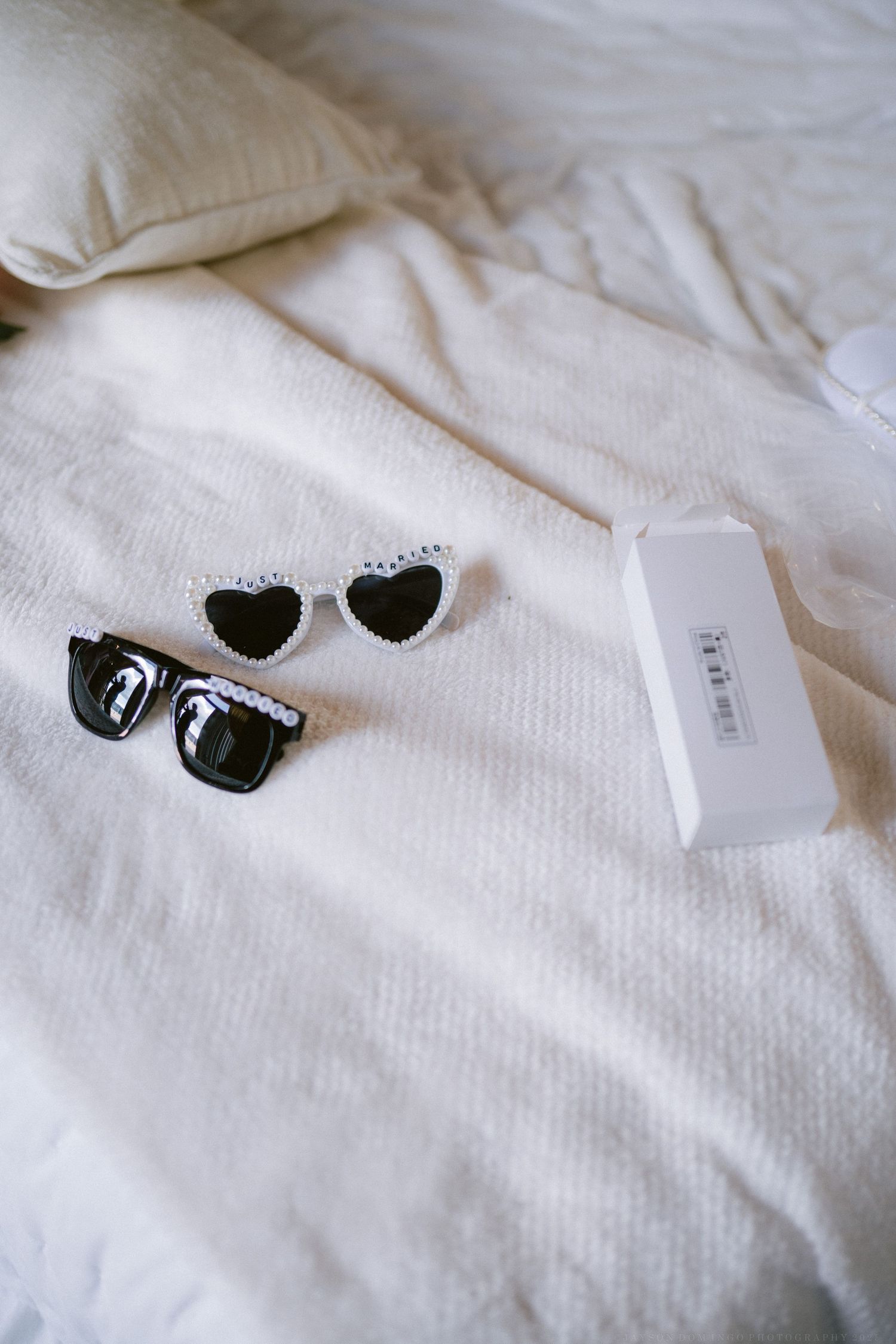 Two pairs of sunglasses, including heart-shaped frames, displayed on white bedding.